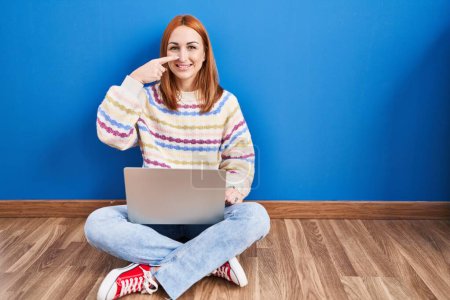 Photo for Young woman using laptop at home sitting on the floor pointing with hand finger to face and nose, smiling cheerful. beauty concept - Royalty Free Image