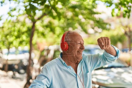 Téléchargez les photos : Homme âgé aux cheveux gris écoutant de la musique et dansant dans la rue - en image libre de droit