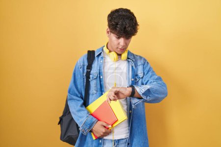 Photo for Hispanic teenager wearing student backpack and holding books looking at the watch time worried, afraid of getting late - Royalty Free Image