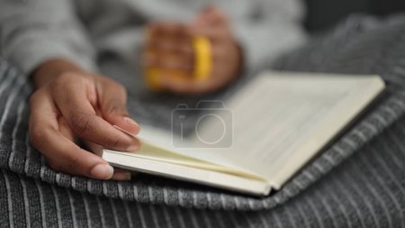 Photo for African american woman reading book sitting on sofa at home - Royalty Free Image