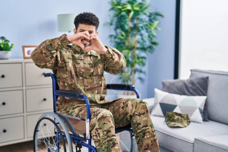 Photo for Arab man wearing camouflage army uniform sitting on wheelchair smiling in love doing heart symbol shape with hands. romantic concept. - Royalty Free Image