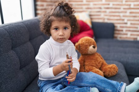 Photo for Adorable hispanic girl holding pencils sitting on sofa at home - Royalty Free Image