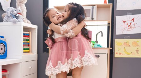 Foto de Adorables chicas gemelas jugando con la cocina de juego abrazándose en el jardín de infantes - Imagen libre de derechos