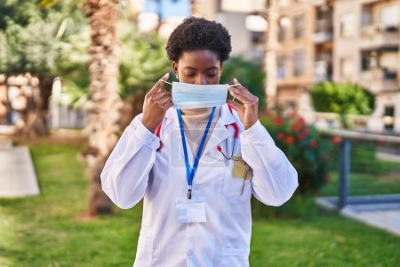 Téléchargez les photos : Femme afro-américaine portant un uniforme de médecin et un masque médical debout au parc - en image libre de droit