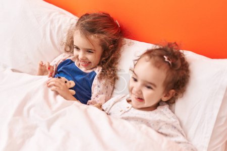Foto de Adorables chicas sonriendo confiadas acostadas en la cama en el dormitorio - Imagen libre de derechos