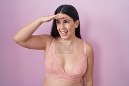 Photo for Young hispanic woman wearing pink bra very happy and smiling looking far away with hand over head. searching concept. - Royalty Free Image