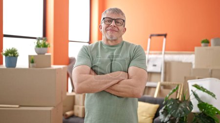 Téléchargez les photos : Homme aux cheveux gris d'âge moyen souriant confiant debout avec les bras croisés geste à la nouvelle maison - en image libre de droit