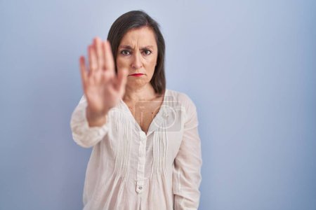 Photo for Middle age hispanic woman standing over blue background doing stop sing with palm of the hand. warning expression with negative and serious gesture on the face. - Royalty Free Image