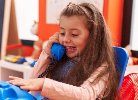 Photo for Adorable hispanic girl playing telephone toy sitting on table at kindergarten - Royalty Free Image