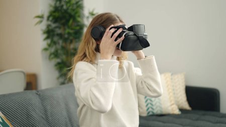 Photo for Young blonde woman playing video game using virtual reality glasses at home - Royalty Free Image