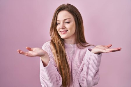 Téléchargez les photos : Young caucasian woman standing over pink background smiling showing both hands open palms, presenting and advertising comparison and balance - en image libre de droit