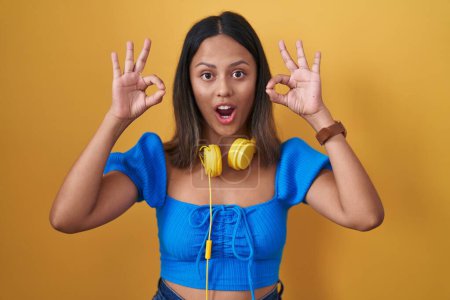 Photo for Hispanic young woman standing over yellow background looking surprised and shocked doing ok approval symbol with fingers. crazy expression - Royalty Free Image