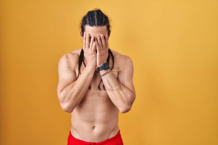 Photo for Hispanic man with long hair standing shirtless over yellow background with sad expression covering face with hands while crying. depression concept. - Royalty Free Image