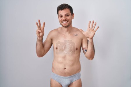 Photo for Young hispanic man standing shirtless wearing underware showing and pointing up with fingers number eight while smiling confident and happy. - Royalty Free Image