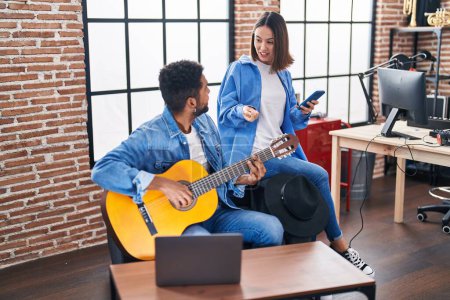 Téléchargez les photos : Musiciens hommes et femmes jouant de la guitare classique avec smartphone au studio de musique - en image libre de droit