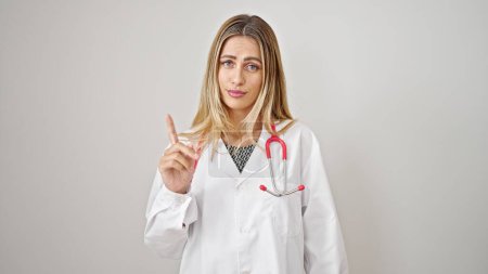 Foto de Mujer joven rubia médico de pie con expresión seria diciendo no con el dedo sobre el fondo blanco aislado - Imagen libre de derechos