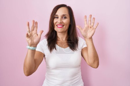 Téléchargez les photos : Femme brune d'âge moyen debout sur fond rose montrant et pointant vers le haut avec les doigts numéro neuf tout en souriant confiant et heureux. - en image libre de droit
