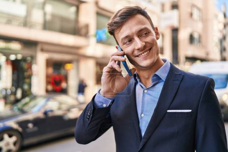 Téléchargez les photos : Jeune homme d'affaires travailleur souriant confiant parler sur smartphone à la rue - en image libre de droit