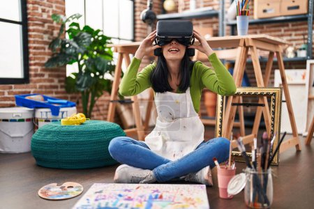 Foto de Joven artista caucásica sentada en el suelo usando gafas de realidad virtual en un estudio de arte - Imagen libre de derechos