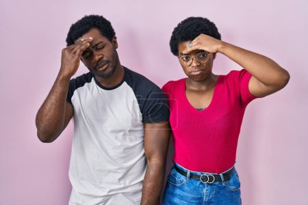 Foto de Joven pareja afroamericana de pie sobre fondo rosa preocupada y estresada por un problema con la mano en la frente, nerviosa y ansiosa por la crisis - Imagen libre de derechos