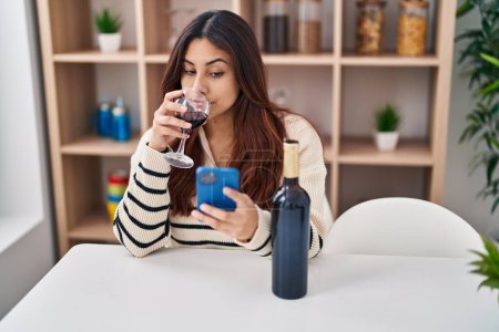 Téléchargez les photos : Jeune femme hispanique utilisant smartphone et boire du vin à la maison - en image libre de droit