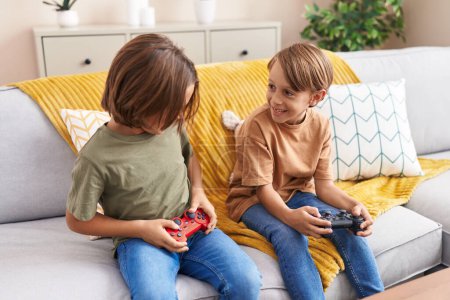 Foto de Adorables chicos jugando videojuegos sentados en el sofá en casa - Imagen libre de derechos
