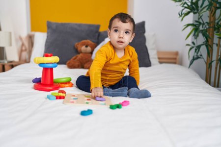 Photo for Adorable hispanic boy playing with maths puzzle game sitting on bed at bedroom - Royalty Free Image