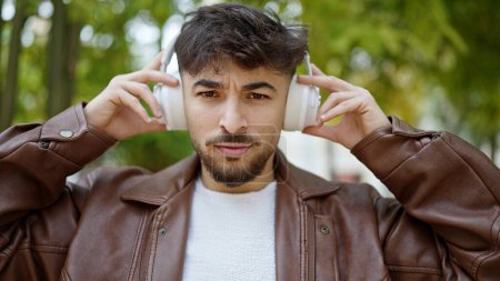 Foto de Hombre árabe joven escuchando música con expresión relajada en el parque - Imagen libre de derechos