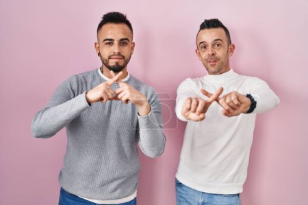 Photo for Homosexual couple standing over pink background rejection expression crossing fingers doing negative sign - Royalty Free Image