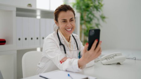 Photo for Middle age hispanic woman wearing doctor uniform having video call at clinic - Royalty Free Image