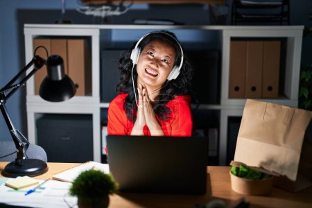 Téléchargez les photos : Jeune femme asiatique travaillant au bureau avec ordinateur portable la nuit suppliant et priant avec les mains ainsi que l'expression de l'espoir sur le visage très émotionnel et inquiet. mendier. - en image libre de droit