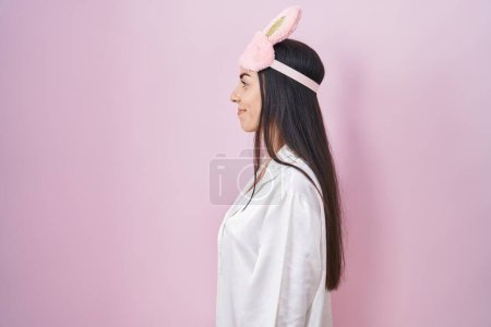 Photo for Young brunette woman wearing sleep mask and pajama looking to side, relax profile pose with natural face with confident smile. - Royalty Free Image