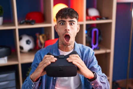 Photo for Young hispanic man wearing virtual reality glasses afraid and shocked with surprise and amazed expression, fear and excited face. - Royalty Free Image