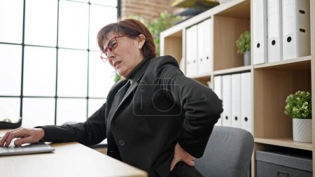 Foto de Mujer hispana madura trabajadora de negocios que sufre de dolor de espalda en la oficina - Imagen libre de derechos