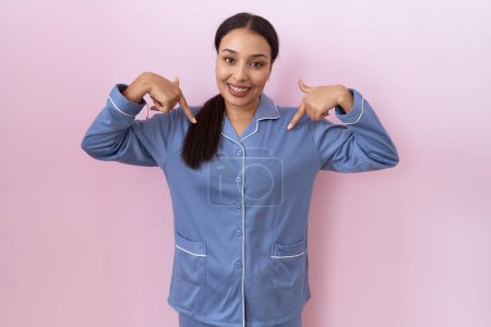 Photo for Young arab woman wearing blue pajama looking confident with smile on face, pointing oneself with fingers proud and happy. - Royalty Free Image