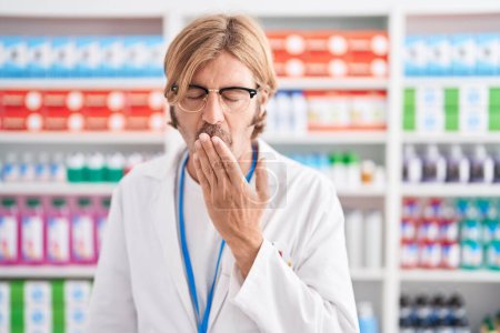 Photo for Caucasian man with mustache working at pharmacy drugstore bored yawning tired covering mouth with hand. restless and sleepiness. - Royalty Free Image
