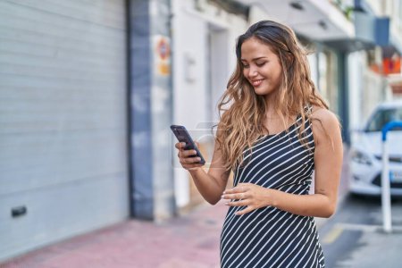 Téléchargez les photos : Jeune belle femme hispanique souriant confiant en utilisant smartphone à la rue - en image libre de droit