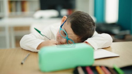 Téléchargez les photos : Adorable hispanique garçon étudiant écriture notes fatigué à salle de classe - en image libre de droit