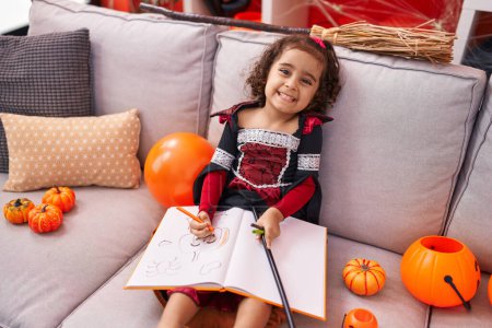 Photo for Adorable hispanic girl wearing halloween costume drawing on notebook at home - Royalty Free Image