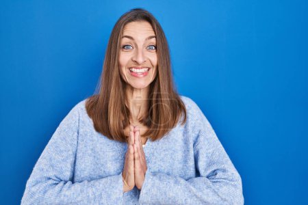Photo for Young woman standing over blue background praying with hands together asking for forgiveness smiling confident. - Royalty Free Image