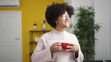 Téléchargez les photos : Jeune femme afro-américaine buvant du thé assis sur le canapé à la maison - en image libre de droit