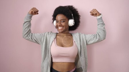 Foto de Mujer afroamericana escuchando música haciendo un gesto fuerte sobre un fondo rosa aislado - Imagen libre de derechos