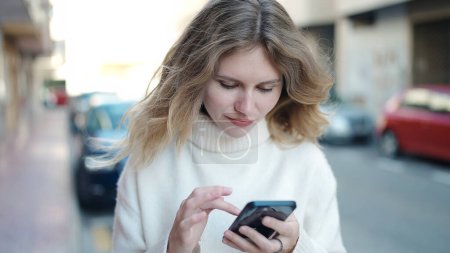 Photo for Young blonde woman using smartphone standing at street - Royalty Free Image