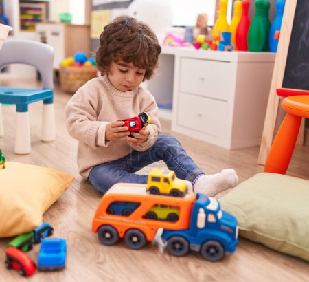 Foto de Adorable niño hispano jugando con juguete de coche sentado en el suelo en el jardín de infantes - Imagen libre de derechos
