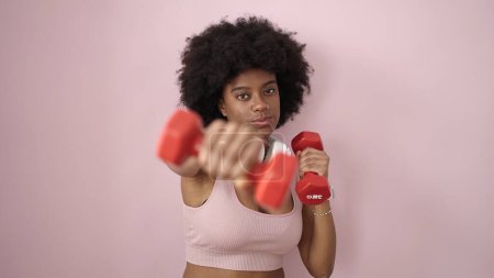 Téléchargez les photos : Femme afro-américaine utilisant haltères formation sur fond rose isolé - en image libre de droit
