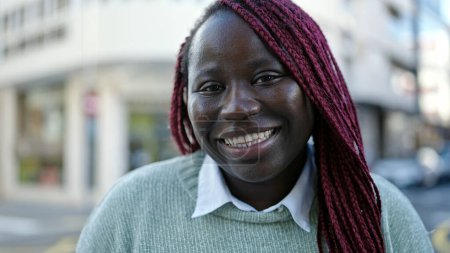Téléchargez les photos : Femme africaine avec les cheveux tressés souriant confiant à la rue - en image libre de droit