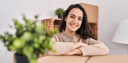 Photo for Young hispanic woman smiling confident leaning on package at new home - Royalty Free Image