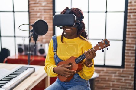 Foto de Músico afroamericano tocando ukelele usando gafas de realidad virtual en un estudio de música - Imagen libre de derechos