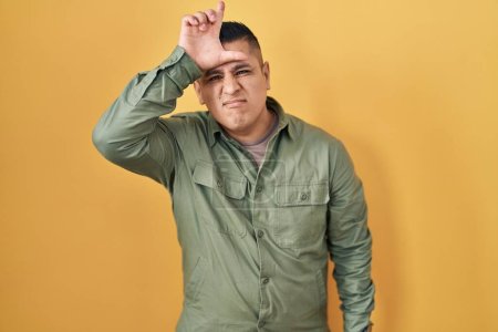 Téléchargez les photos : Jeune homme hispanique debout sur fond jaune se moquant des gens avec les doigts sur le front faisant geste de perdant se moquant et insultant. - en image libre de droit