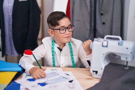 Photo for Young hispanic kid at tailor room pointing thumb up to the side smiling happy with open mouth - Royalty Free Image